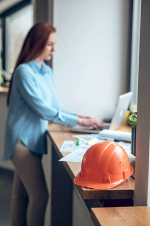 Protective helmet on windowsill and woman working on laptop