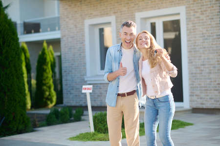 Joyful woman showing key and man near houseの写真素材