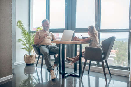 A man and his daughter sitting at the table, man working , his daughter eatingの写真素材