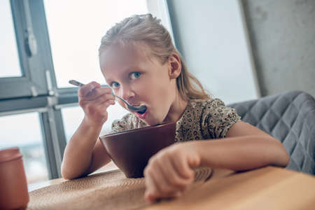 A cute blone girl eating her breakfast and looking involvedの写真素材