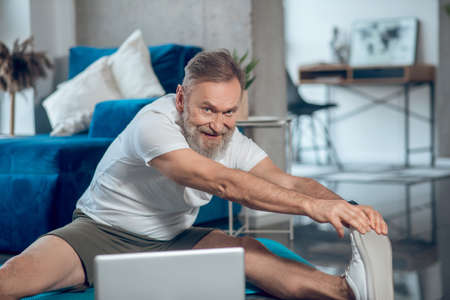 A mature man having online workout and stretchingの写真素材