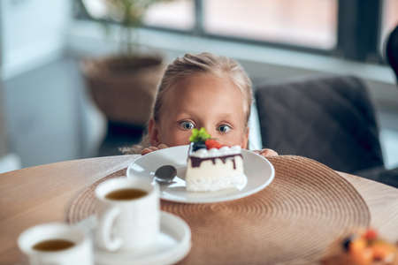A cute blonde girl looking anticipated while looking at the slice of cake