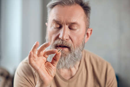 A bearded man holding a pill and looking at itの写真素材