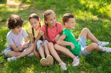Smiling boys and girls sitting on green lawn