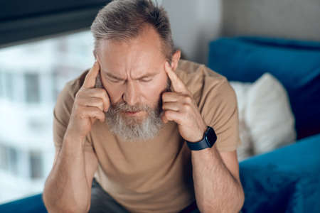 A mature bearded man suffering from a headache
