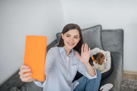 A cute young woman making selfie with her puppy and looking happy