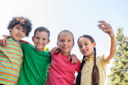 Embracing smiling school age friends outdoorsの写真素材