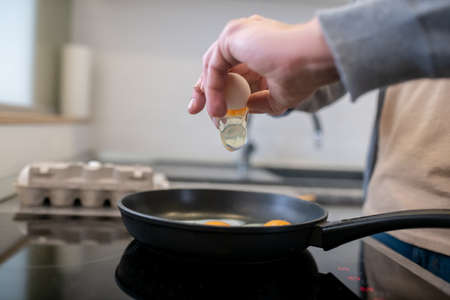 A gray-haired man cooking omlette in the kitchenの写真素材