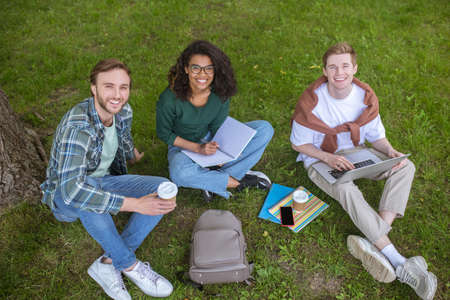 Young guys and a girl sitting on the grass near the college building