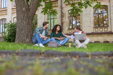 Young guys and a girl sitting on the grass near the college building