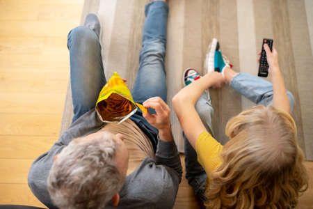 A blonde teen sitting on the floor with her dad and eating chips