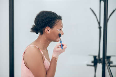 A pretty curly-haired woman doing make and looking pleasedの写真素材