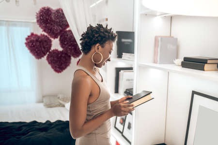 A woman in beige dress talking a book from the shelf