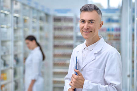 Smiling pharmacist with folder and woman behindの写真素材