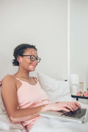 A dark-skinned womant typing on laptop while staying in bedの写真素材