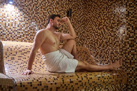 A man in a towel sitting in sauna and having detox sessionの写真素材