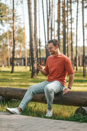 Smiling man with smartphone sitting in natureの写真素材