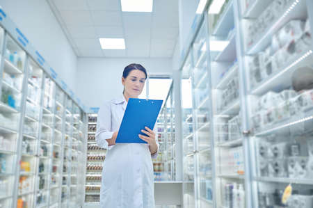 Woman in white coat with folder in pharmacyの写真素材