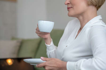 Blonde woman sitting on the sofa and having teaの写真素材