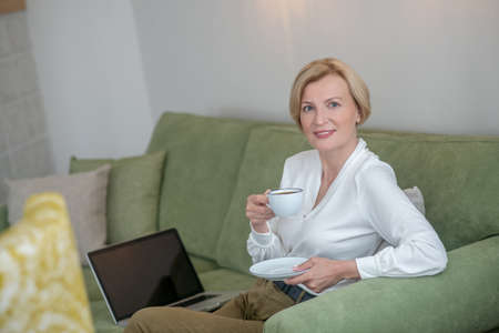 Blonde woman sitting on the sofa and having teaの写真素材