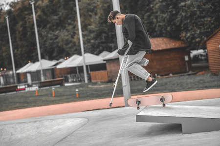 Guy on crutches while jumping on skateboard from springboardの写真素材