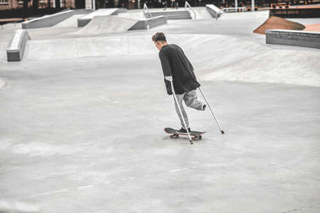 Back view of guy on crutches gliding on skateboardの写真素材
