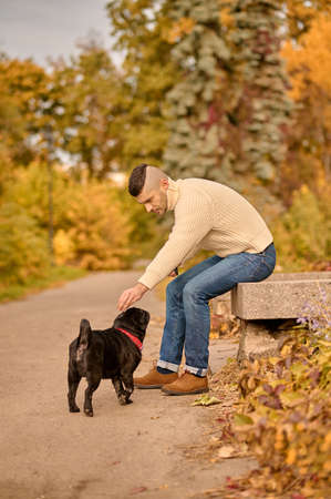 A man in beige turtleneck resting in the park with his petの写真素材