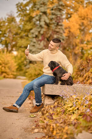 A man in beige turtleneck resting in the park with his petの写真素材