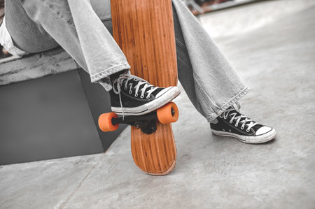 Legs near skateboard of person sitting in parkの写真素材