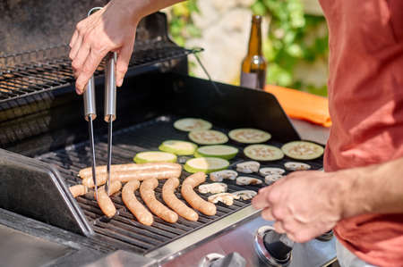 A man cooking grilled sausages and vegetablesの写真素材