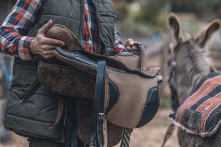 A man putting a saddle on a donkeys backの写真素材