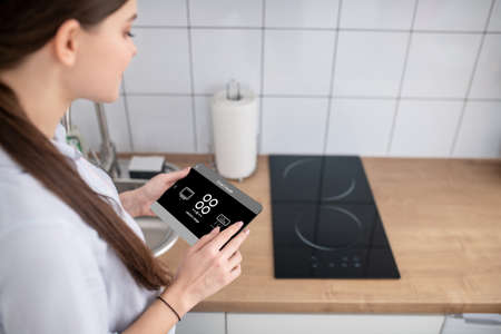 Housewife turning on the cooktop using a gadgetの写真素材