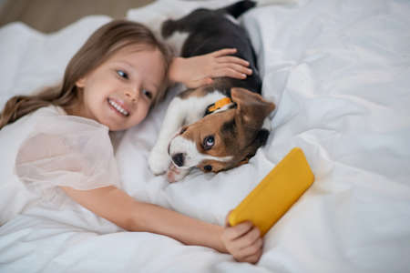 Pretty little girl taking selfies with her funny four-legged friendの写真素材