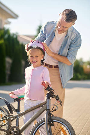 A man putting protective helmet on his daughters head before riding a bikeの写真素材