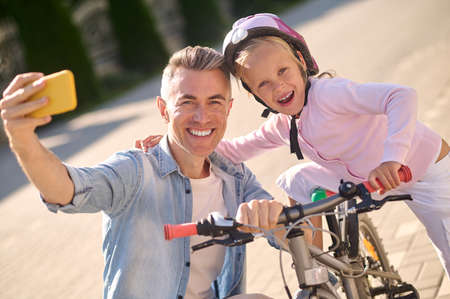 A smiling man making selfie with his kid on a bikeの写真素材
