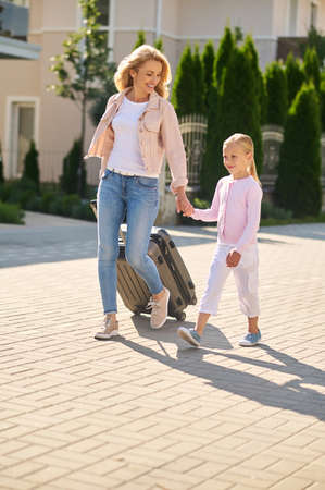 Blonde woman carrying a suitcase and holding her daughters handの写真素材