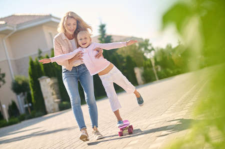 Mom helping her daughter ride a skateboardの写真素材