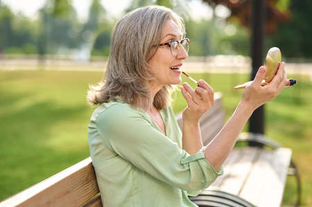 Woman looking in mirror applying lipstick on lipsの写真素材