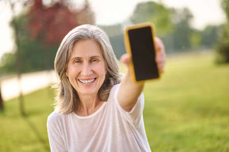 Woman showing smartphone screen outstretching hand to cameraの写真素材