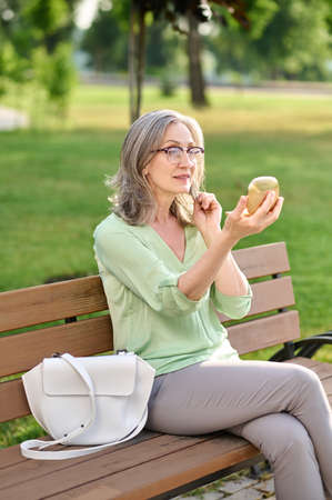 Woman looking in mirror sitting on benchの写真素材