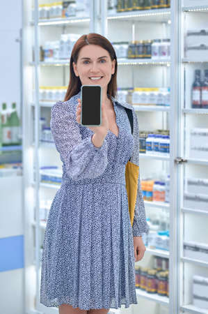 Smiling woman in na dress holding a smartphoneの写真素材