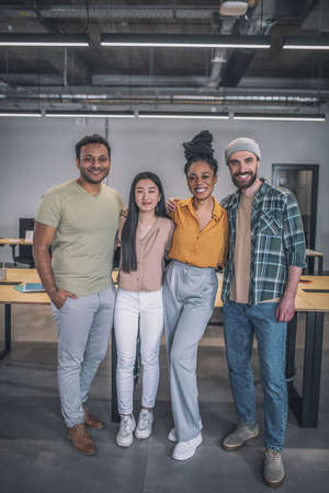 Four interracial young people standing hugging at officeの写真素材