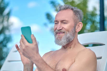 Bearded mature man sunbathing and typing messageの写真素材