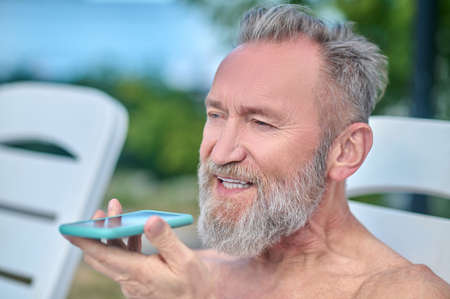 Bearded mature man sunbathing and recording a voice messageの写真素材