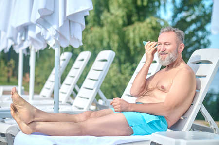 Bearded mature man sunbathing and listening to a voice messageの写真素材