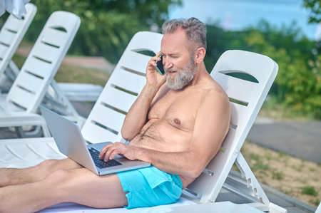 Bearded man working on a beach and having a phone callの写真素材