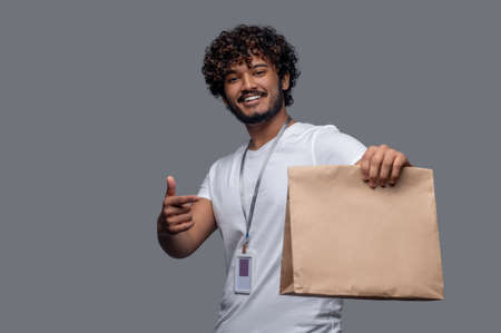 Smiling deliveryman in the T-shirt holding a paper bagの写真素材