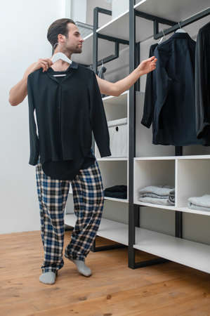Man in plaid home pants choosing a shirt to wearの写真素材