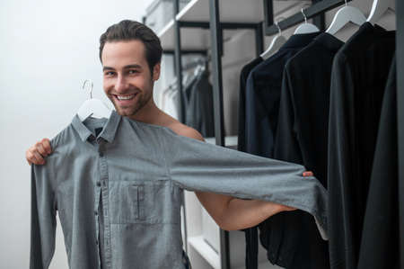 A man choosing clothing and holding a grey shirt in handsの写真素材