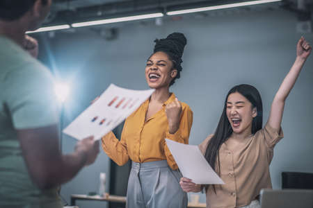 Emotional african american and asian girls rejoicing in officeの写真素材